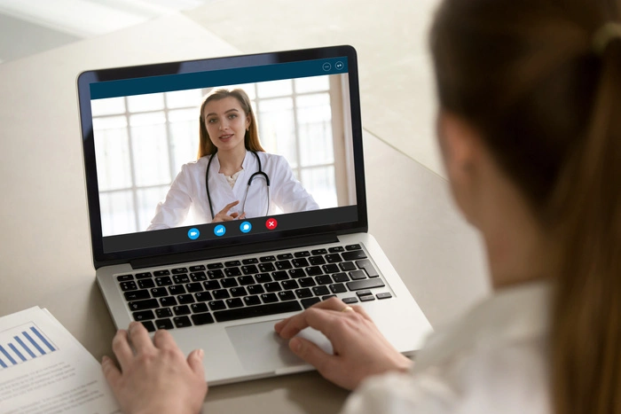 Shoulder view young woman consulting with family therapist doctor general practitioner online via video call on laptop after feeling first virus illness symptoms