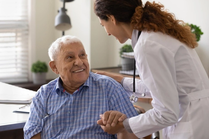Close up caring nurse holding smiling mature patient hand at meeting in hospital