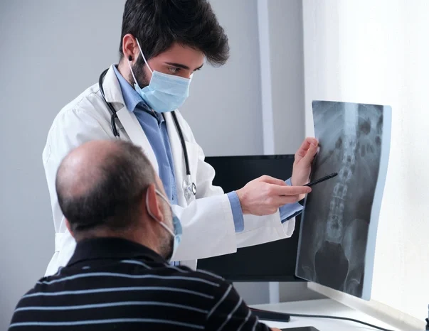Young doctor examining x-ray of a senior patient backbone