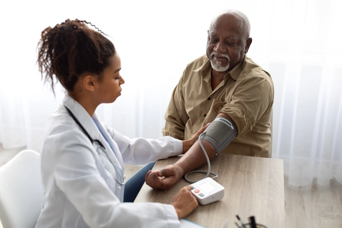 Young Female Medical Worker Measuring Arterial Blood Pressure Of Senior Black Man Using Cuff