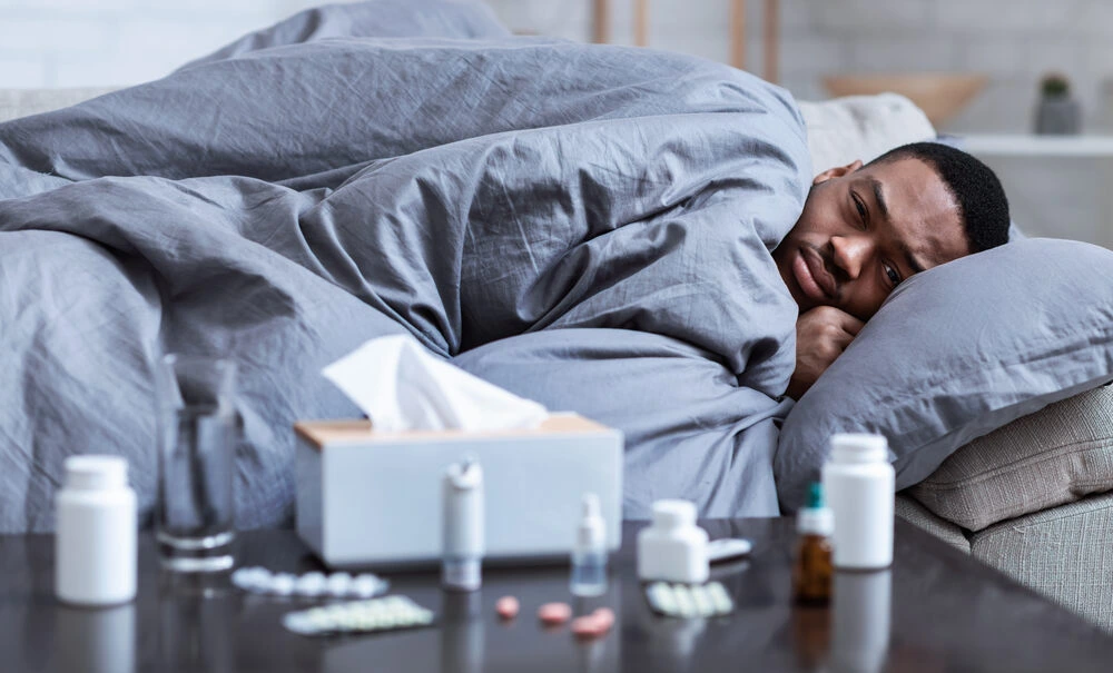 Sick Guy Having Fever And Chills Lying Wrapped In Blanket On Couch At Home